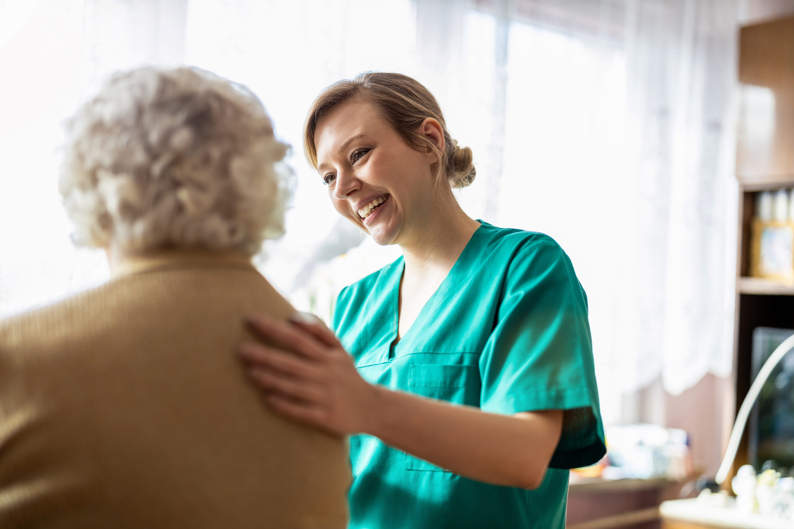 Pflegekraft mit einer Patientin Pflegekraft legt fröhlich und freundlich ihre Hand auf die Schulter einer älteren Patientin.