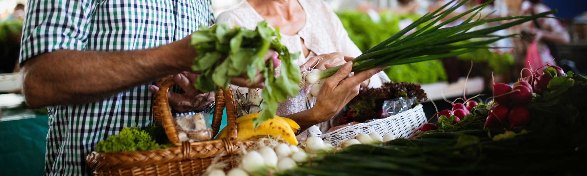 Seniorenehepaar ist gemeinsam auf dem Wochenmarkt und kauft regionales Obst und Gemüse ein.